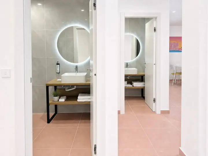 Two open bathroom doors, each with a round backlit mirror and basin