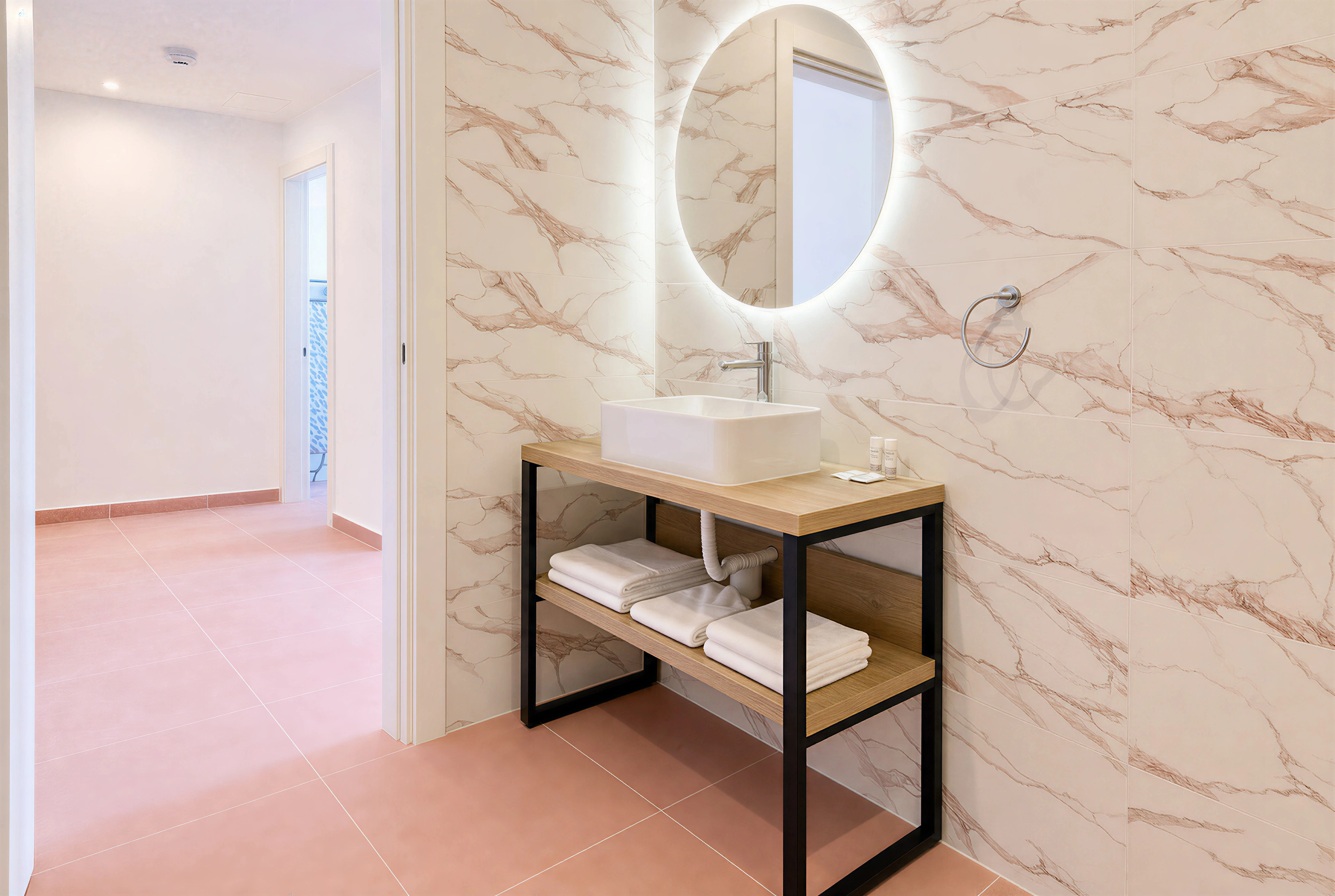 Bathroom with round backlit mirror and pink-veined marble walls at The Flamingo Apartments