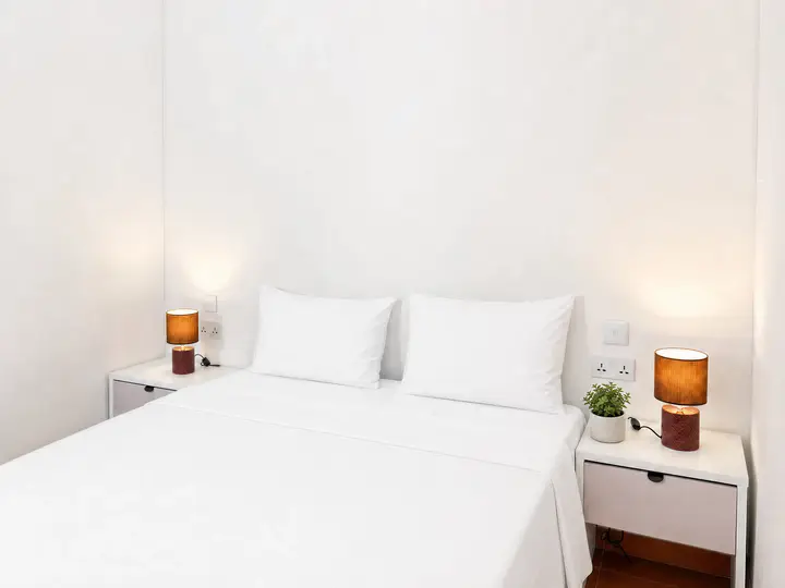Double bed with white linen between two bedside tables with lit lamps