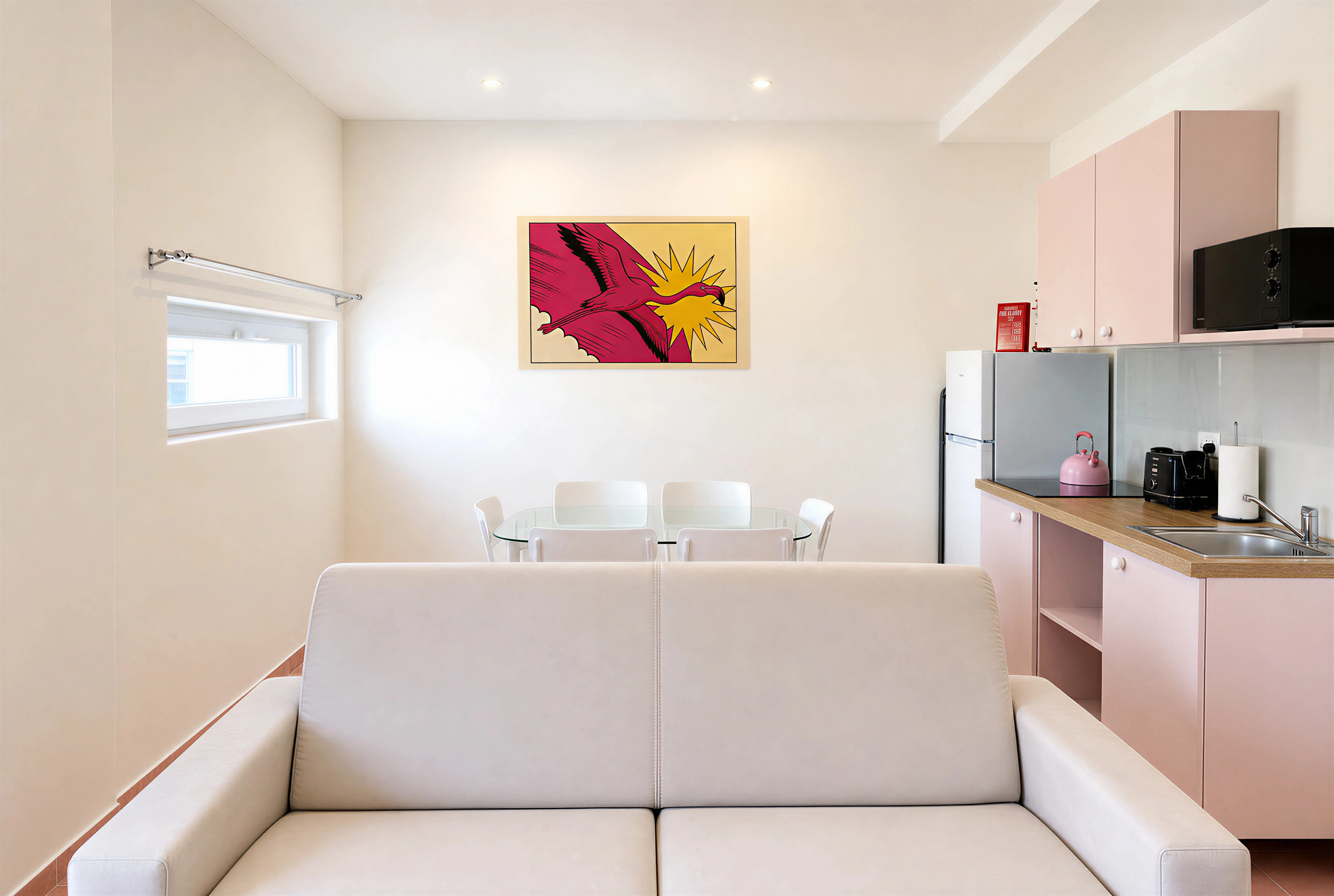 Open-plan living, kitchen and dining area with cream sofa, glass dining table and pink kitchen units — 2-bedroom Flamingo apartment, Paceville Malta
